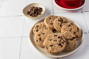 Plate of chocolate chip cookies with extra chocolate chips on side, set on a tiled background
