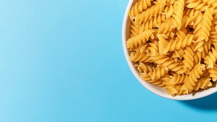 Uncooked fusilli pasta spirals in a white bowl on a blue background. Copy space