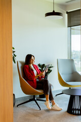 Young professional woman working on tablet in modern office seating area in morning light