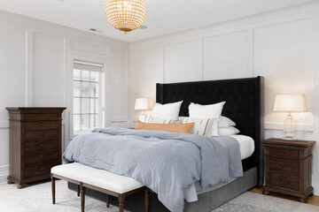 A bedroom detail with cozy decor, wainscoting walls, and a gold and crystal chandelier hanging...