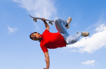 young man posing happy with skateboard in hand background blue and cloudy. youth sports and...