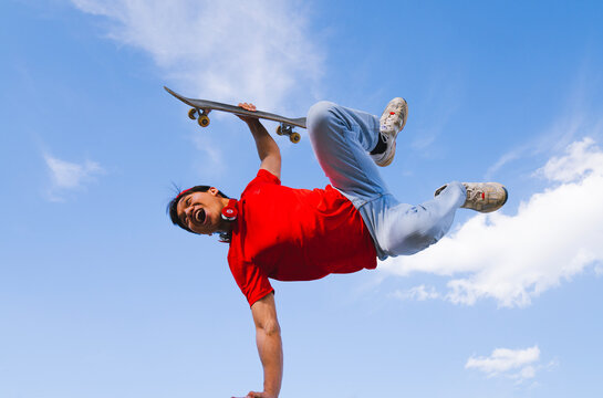 young man posing happy with skateboard in hand background blue and cloudy. youth sports and entertainment concept