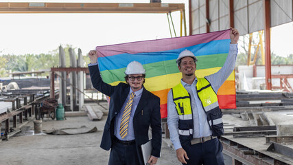 Two engineers with safety hat hold a flag to express their support to LGBT right in a construction...
