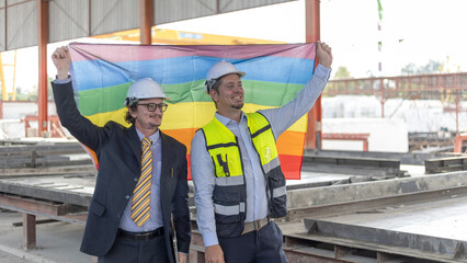 Two engineers with safety hat hold a flag to express their support to LGBT right in a construction...