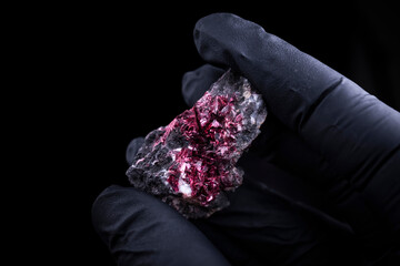 Someone with black gloves holding an eryhtrite, mineral specimen from Morocco.