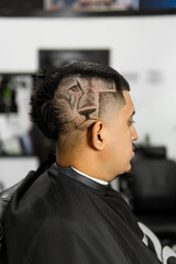 Side view of a young man with a modern and artistic haircut, showcasing geometric designs, in a professional barbershop setting.