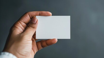 Obraz premium Human hand holding a blank white card against a grey background
