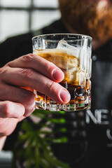 Close-up of a person’s hand holding a glass of cocktail with ice. The focus is on the drink, with a blurred background. Perfect for beverage and lifestyle concepts