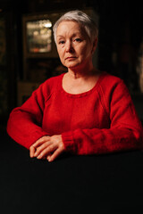 Vertical portrait of grey-haired middle-aged woman in casual red sweater looking at camera with...