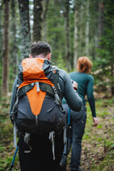 A couple is hiking on a trail through the forest, surrounded by natural landscape. They carry...