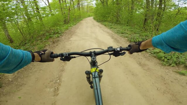 Spectacular extreme video of a mountain bike ride. Cyclist wearing a blue long sleeved shirt and gloves riding on a dirt road in the woods. First person view