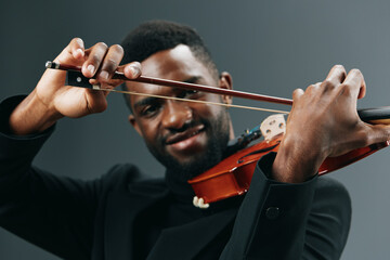 Elegant African American Man in Black Suit Playing Violin on Gray Background
