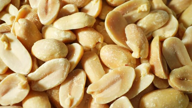 Golden-brown peanuts, split open, expose their creamy kernels beneath a delicate salt dusting. Their rough texture hints at the satisfying crunch within.
