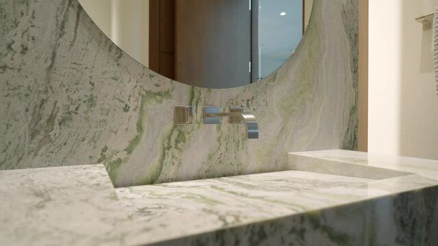 Elegant bathroom vanity with marble countertop and backsplash. Undermount sink with wall-mounted faucet. Round shape mirror indoors