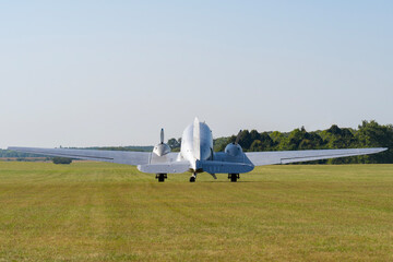 Old metal colored twin engine transport Li-2 airplane in a field from the back