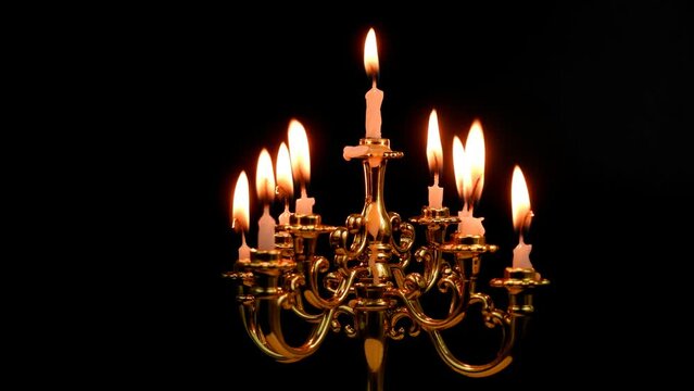 Close-up of rotating candelabra with white burning candles isolated on black.