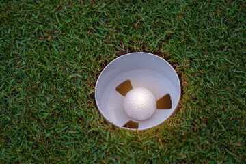 Top view of a golf ball on green course at hole. Golf ball and golf club on green in the evening golf course with sunshine