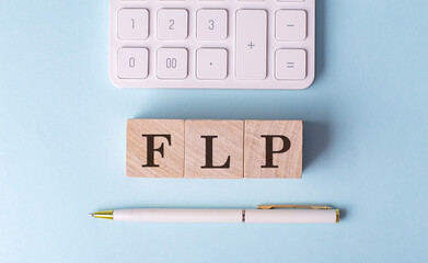 FLP word on wooden block with pen and calculator on blue background