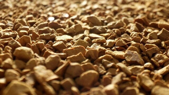 In a mesmerizing close-up, freeze-dried coffee dazzles under the gentle caress of warm light. Each golden-brown morsel resembles a rugged gemstone, forming a captivating mosaic of fragrant allure.
