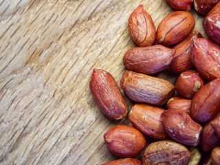 A bunch of peanuts are spread out on a wooden surface. Concept of abundance and variety, as the peanuts come in different sizes and shapes. The wooden surface adds a rustic.