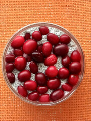 A lot of healthy Chia pudding with coconut milk in a glass containers can with fresh berries as cranberries, cranberry on light red background. Close-up