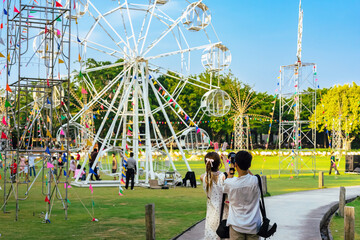 Back view of Asian tourists enjoy outdoor theme park together with beautiful white ferris wheel...