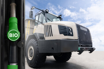 Hand with biofuel filling nozzle on a background of mining truck. Decarbonization of heavy...