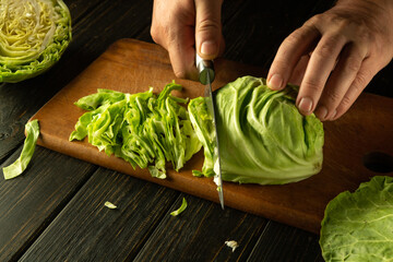 Shredding cabbage with a knife in the hands of a man. The process of preparing sauerkraut on the kitchen table