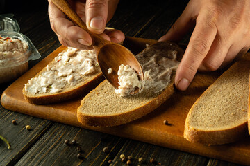 Close-up of a chef hands using a spoon to add grated lard onto rye bread to prepare a delicious sandwich. Healthy fast food concept
