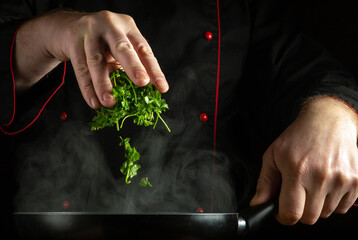A professional chef manually adds fragrant fresh parsley to a hot frying pan. The concept of...