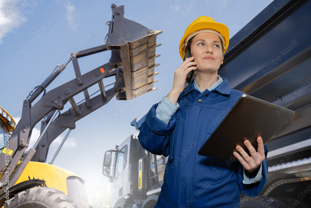 Poster female engineer with a digital tablet on the background of construction machines.