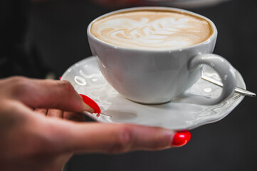 Close-up view of a hand holding a white cup with latte art, suggesting a cozy coffee break or morning routine