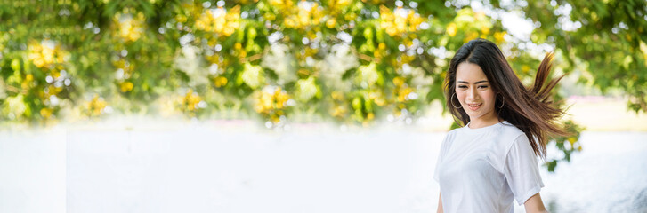Fototapeta premium Banner Happy Relax beautiful asian woman smiling face standing in green park outdoors garden. Young women enjoy nature Lifestyle. Banner woman breathing fresh air breath in green park with copy space