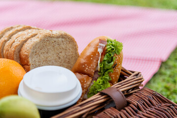 Picnic basket food bread fresh fruit coffee cup orange juice in wood wicker box on red Blanket. Wheat bakery fruit food and drinks in green park outdoor lifestyle. Breakfast healthy appetizer box.