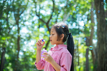 Obraz premium Adorable happy cute girl playful foam bubbles in green playground in summer outdoors. Funny Cheerful girl in the park with happy times.