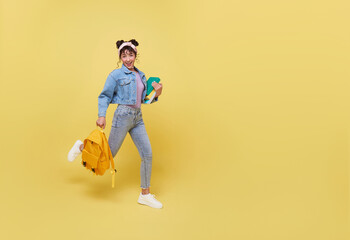 Fototapeta premium Portrait of happy smiling young Asian college student with notebook and backpack walking ready to school isolated on yellow background.