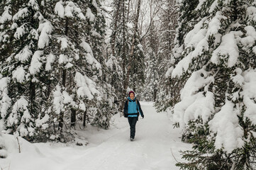 A tourist girl walks through a snow-covered forest with a backpack