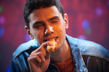 A young guy is eating a piece of pizza in a pizzeria.