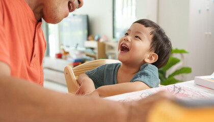 Asian Senior man laughing with Grandson or young boy at home, highlighting learning and bonding...