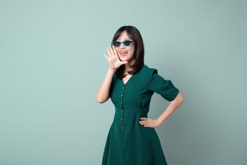 Happy Asian woman with sun glasses shouting above green dress poses against green background blank copy space for advertising content promotion