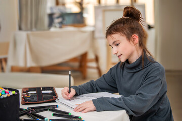 A young girl is sitting at a table with a notebook and a bag of pencils. She is smiling and holding the markers in her hands. The scene suggests that she is enjoying a creative activity