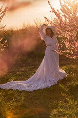 Woman blooming peach orchard. Against the backdrop of a picturesque peach orchard, a woman in a long white dress enjoys a peaceful walk in the park, surrounded by the beauty of nature.