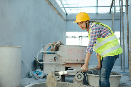 Asian female working in construction site mixing cement, working building innovation on architecture, wearing safety vest and helmet gears.