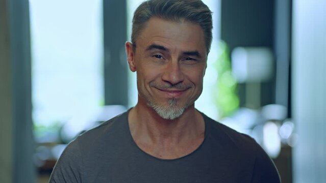 Portrait of a confident man in his 50s showcasing a friendly pleasant smile at home. Happy mid adult, older, senior man with gray hair smiling at home. Blurred background with copy space.