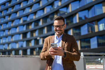 Male professional smiling and texting over smartphone while standing against modern building in city