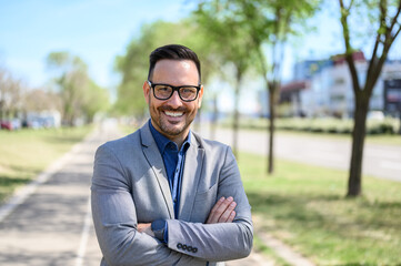 Handsome employee with arms crossed smiling and confidently standing on city street during sunny day