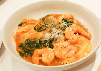 close up of shrimp prawns seafood sauce ravioli with spinach on a white plate. cheese are spread on the top.
