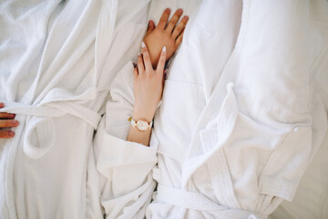 a girl strokes a man's hand while lying on the bed