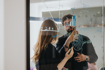 Male and female business professionals brainstorm, discuss, and plan strategies using colorful sticky notes on a glass wall in a modern office environment.