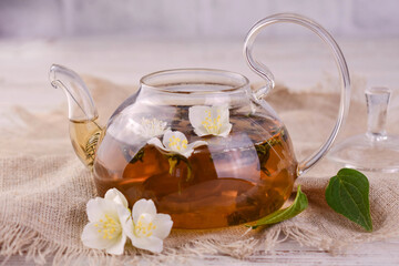 Jasmine tea in a transparent teapot and fresh jasmine flowers.
